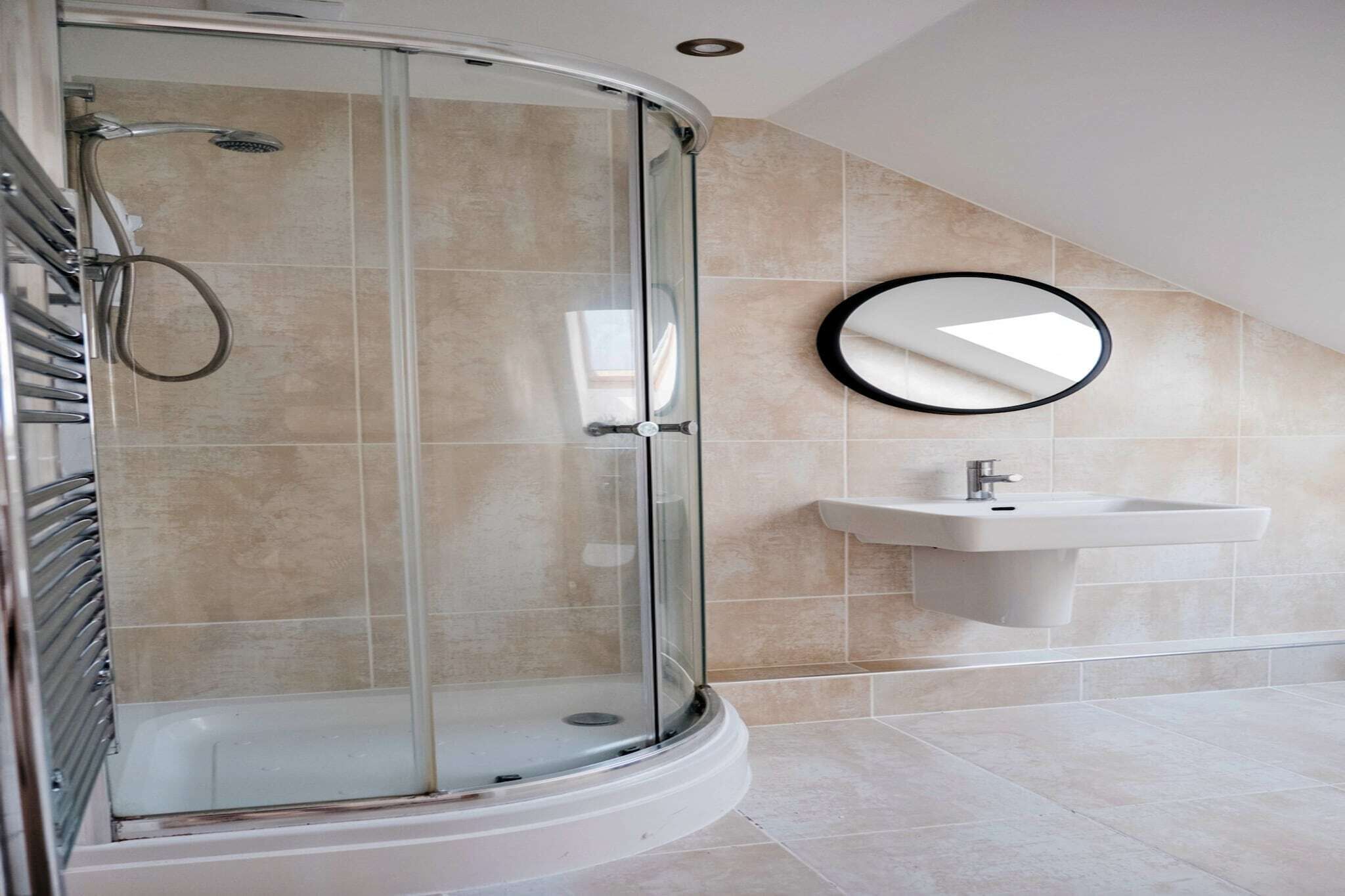 A modern bathroom with a glass-enclosed shower, a wall-mounted sink, and a round mirror.