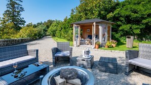 An outdoor seating area with wicker furniture, a fire pit, and a small gazebo. - Castle in Tamar with Pool and Gardens (Saltash)