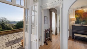 A room with a large window, a piano, and a painting. - Castle in Tamar with Pool and Gardens (Saltash)