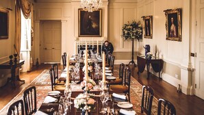 A formal dining room with a long table set for a meal, a chandelier, and framed portraits on the walls. - Castle in Tamar with Pool and Gardens (Saltash)