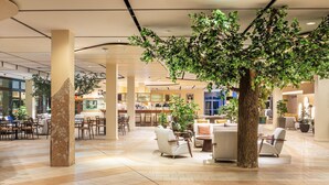 Eine großzügige Lobby mit einem großen Kunstbaum, bequemen Sitzbereichen und einem modernen Innendesign.