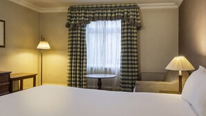 Une chambre d’hôtel avec un grand lit, une table ronde, deux lampes de chevet et une fenêtre avec des rideaux à carreaux.