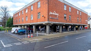 Un bâtiment en briques de deux étages, avec une enseigne indiquant « Hôtel Wessex » et le nom « Hôtel Wessex » écrit sur le côté. Des voitures sont garées devant, et il y a un trottoir pour les piétons.