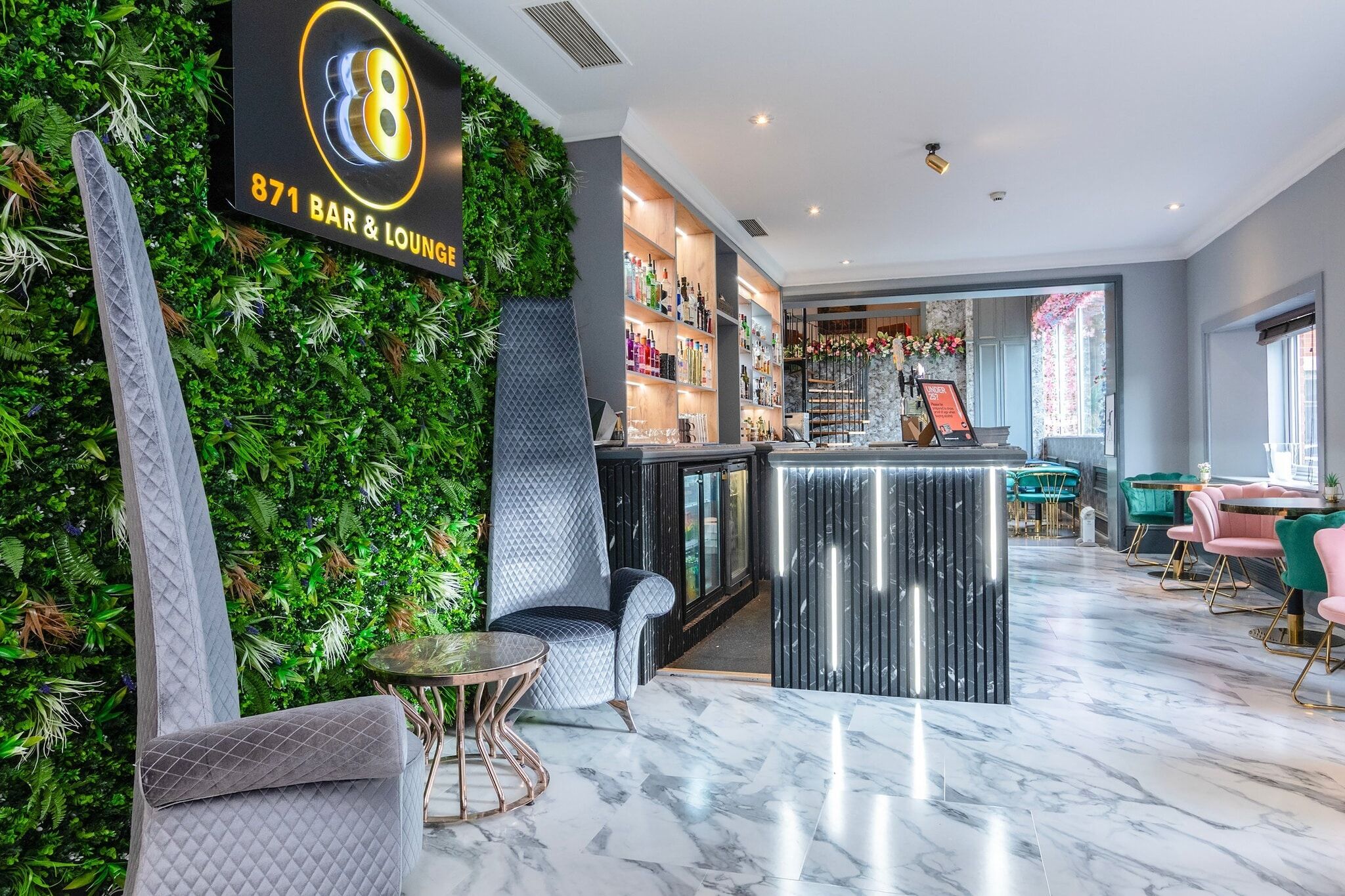 A bar lounge with a green wall, marble flooring, and modern furniture.