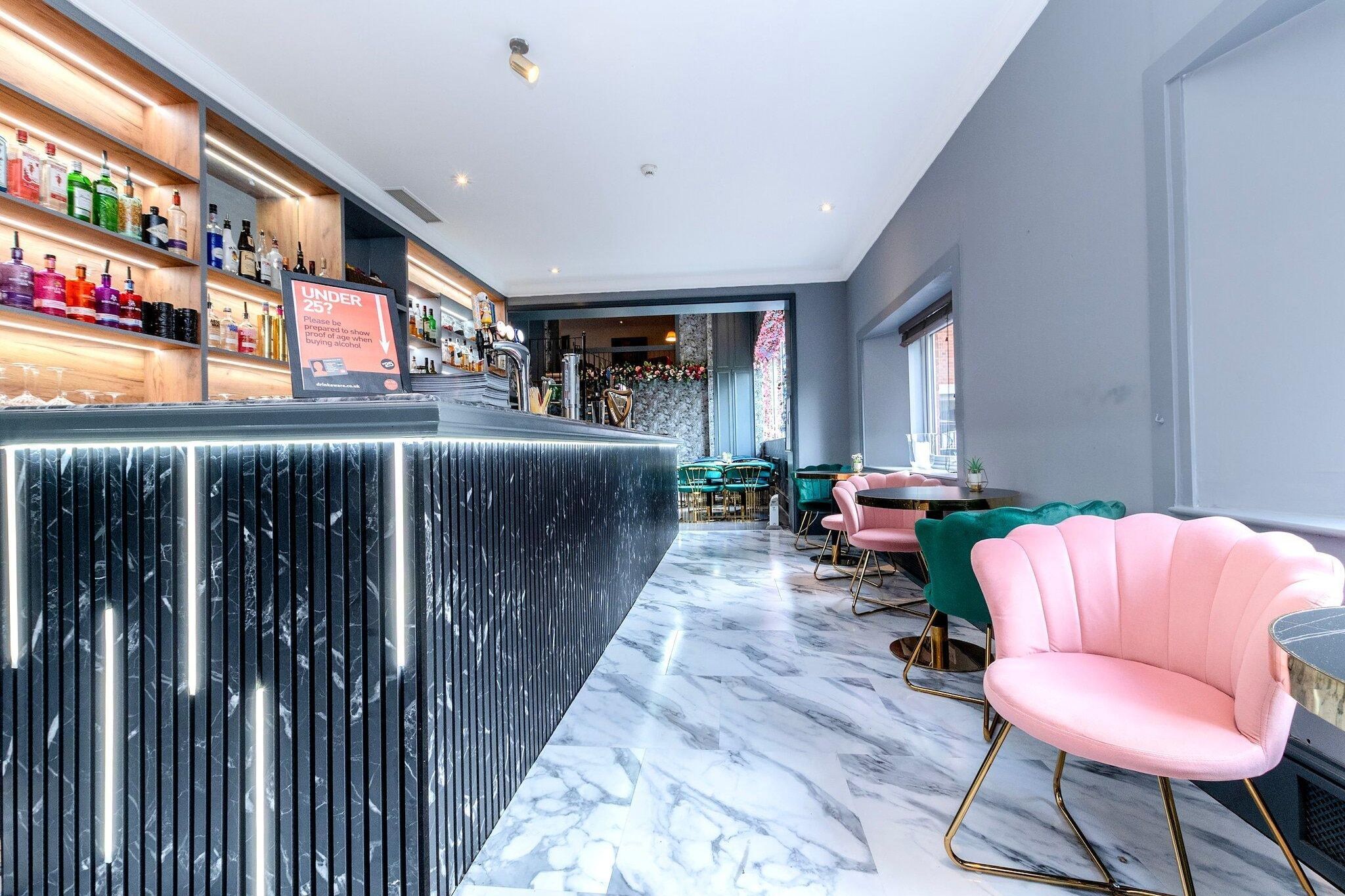 A bar area with a marble countertop, seating with green and pink chairs, and a sign indicating age restriction.