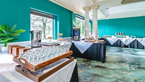Une salle de banquet avec des tables dressées pour un événement formel, un coin café et une vue sur l’extérieur.