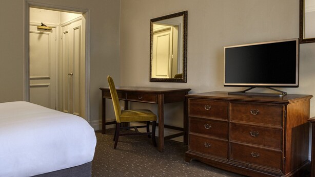 Une chambre d’hôtel comprenant un lit, un bureau avec une chaise, une commode, une télévision et un miroir.