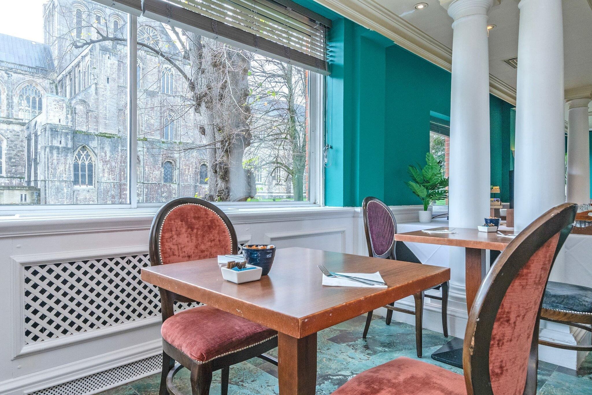 Un coin repas avec une table et des chaises, une vue sur un bâtiment historique à l’extérieur et une fenêtre avec des stores.
