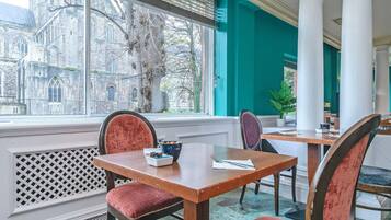 Un coin repas avec une table et des chaises, une vue sur un bâtiment historique à l’extérieur et une fenêtre avec des stores.