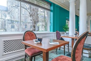 Un comedor con una mesa y sillas, vista a un edificio histórico en el exterior, y una ventana con persianas.