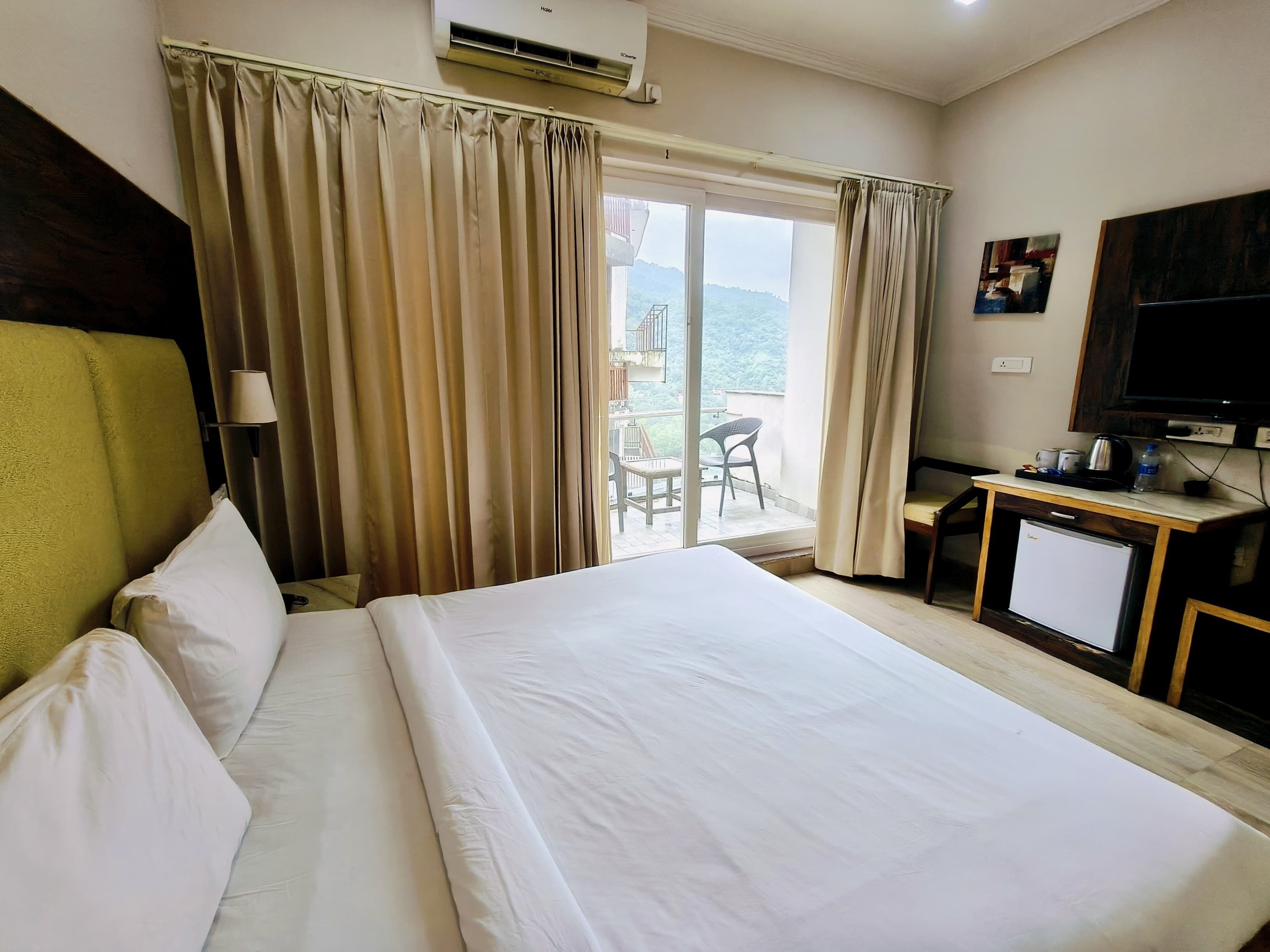 A hotel room with a bed, a desk with a television, and a balcony with a view.