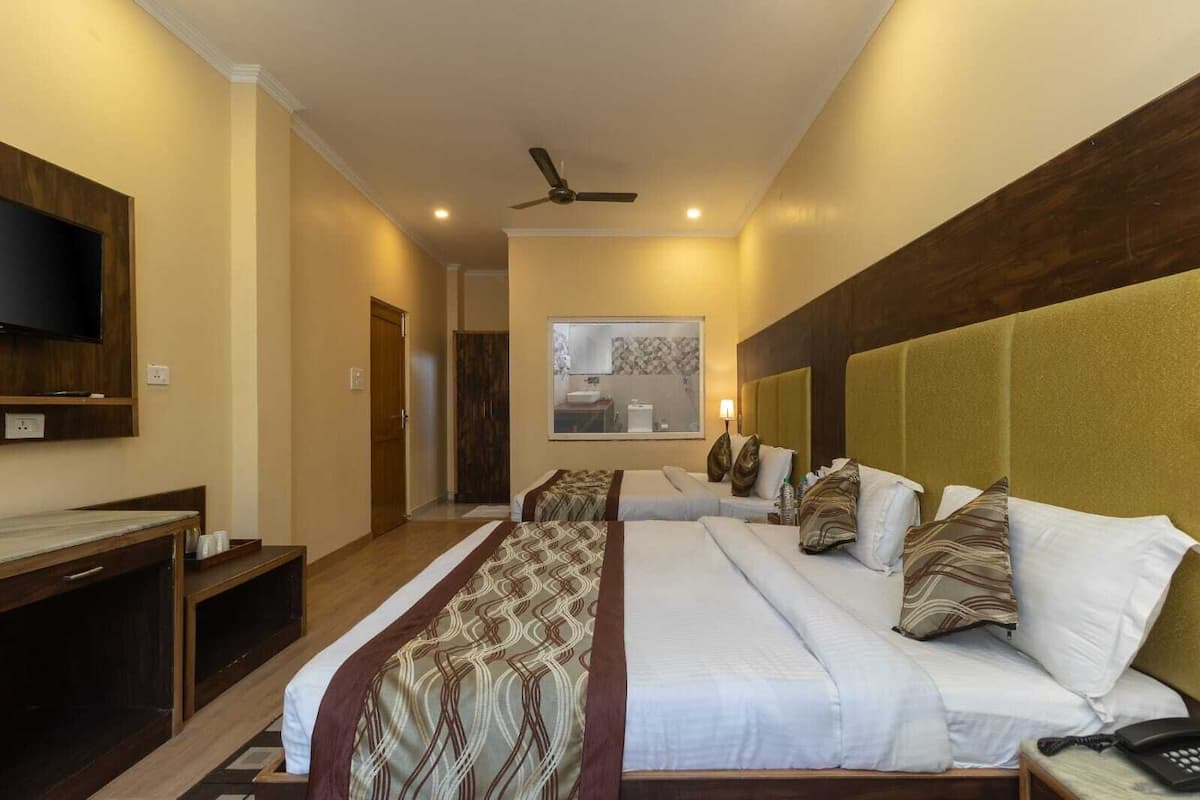 A hotel room with two beds, a TV mounted on the wall, a ceiling fan, and a bathroom visible through the window.