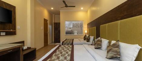 A hotel room with two beds, a TV mounted on the wall, a ceiling fan, and a bathroom visible through the window.