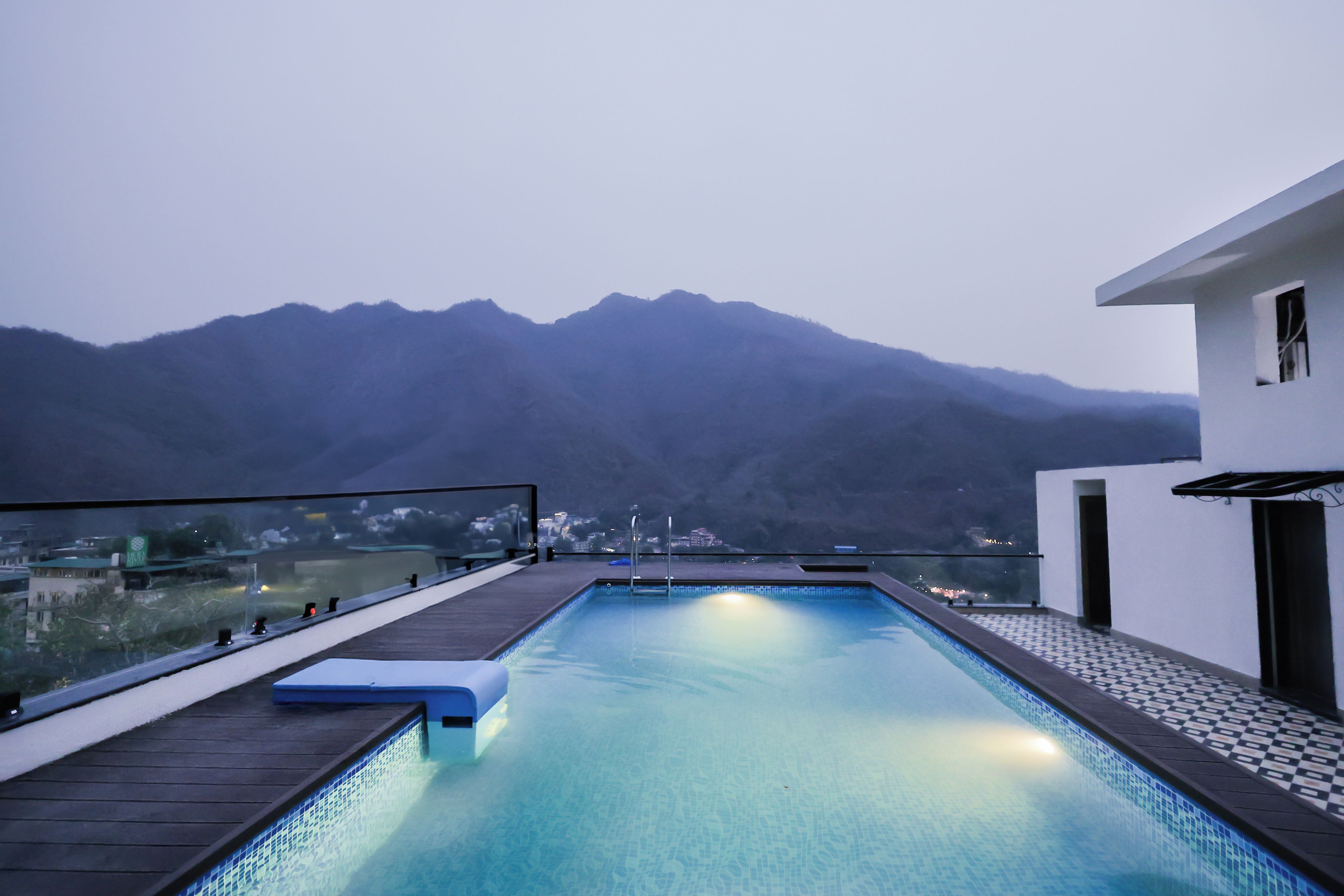 A swimming pool with a view of mountains, a wooden deck, and a modern building.