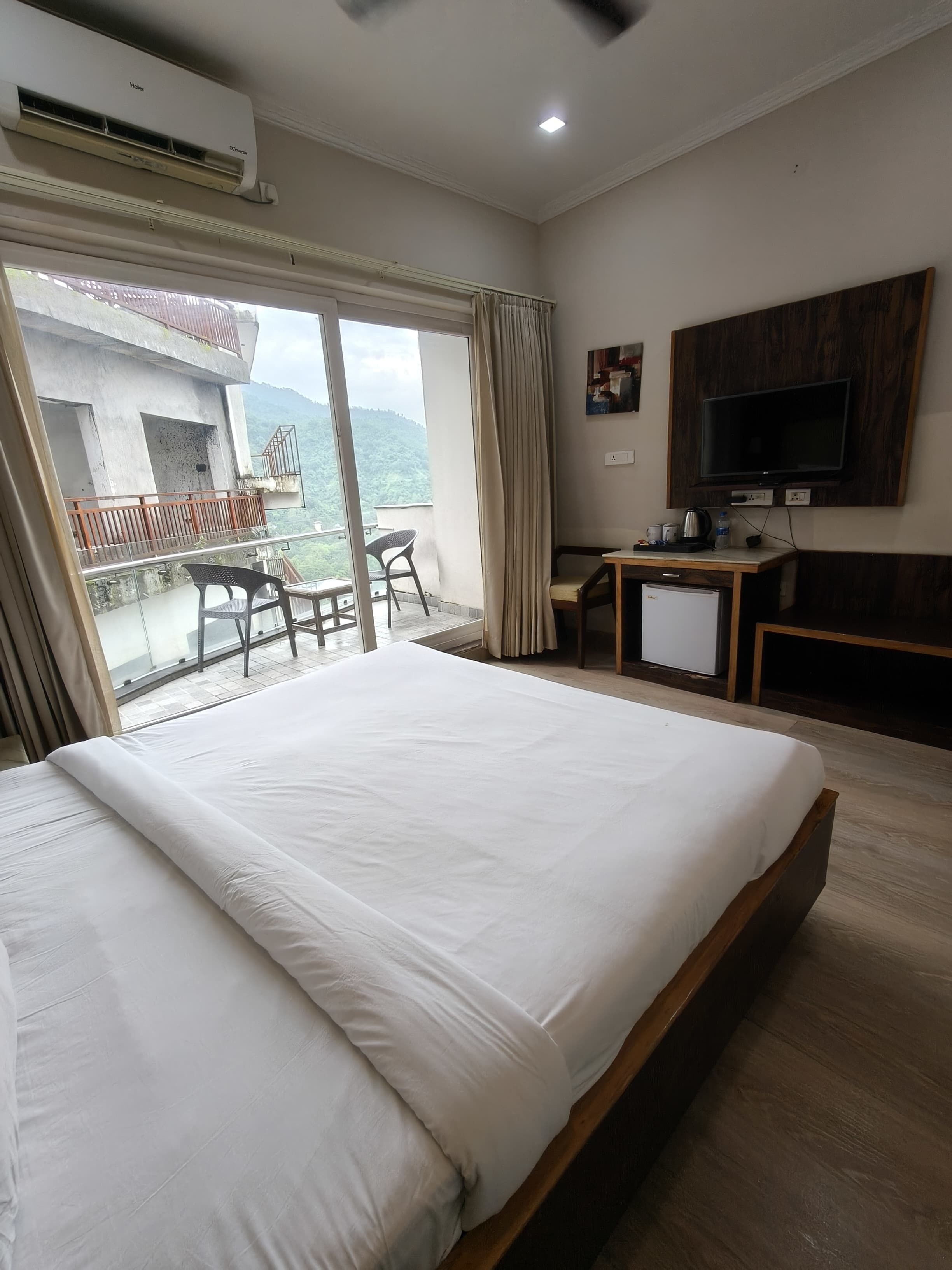 A hotel room with a large bed, a desk, a television, and a balcony with a view of the mountains.