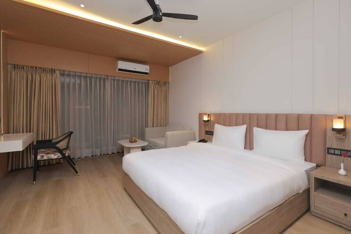 A hotel room with a large bed, a desk, a chair, a small table, and a ceiling fan.