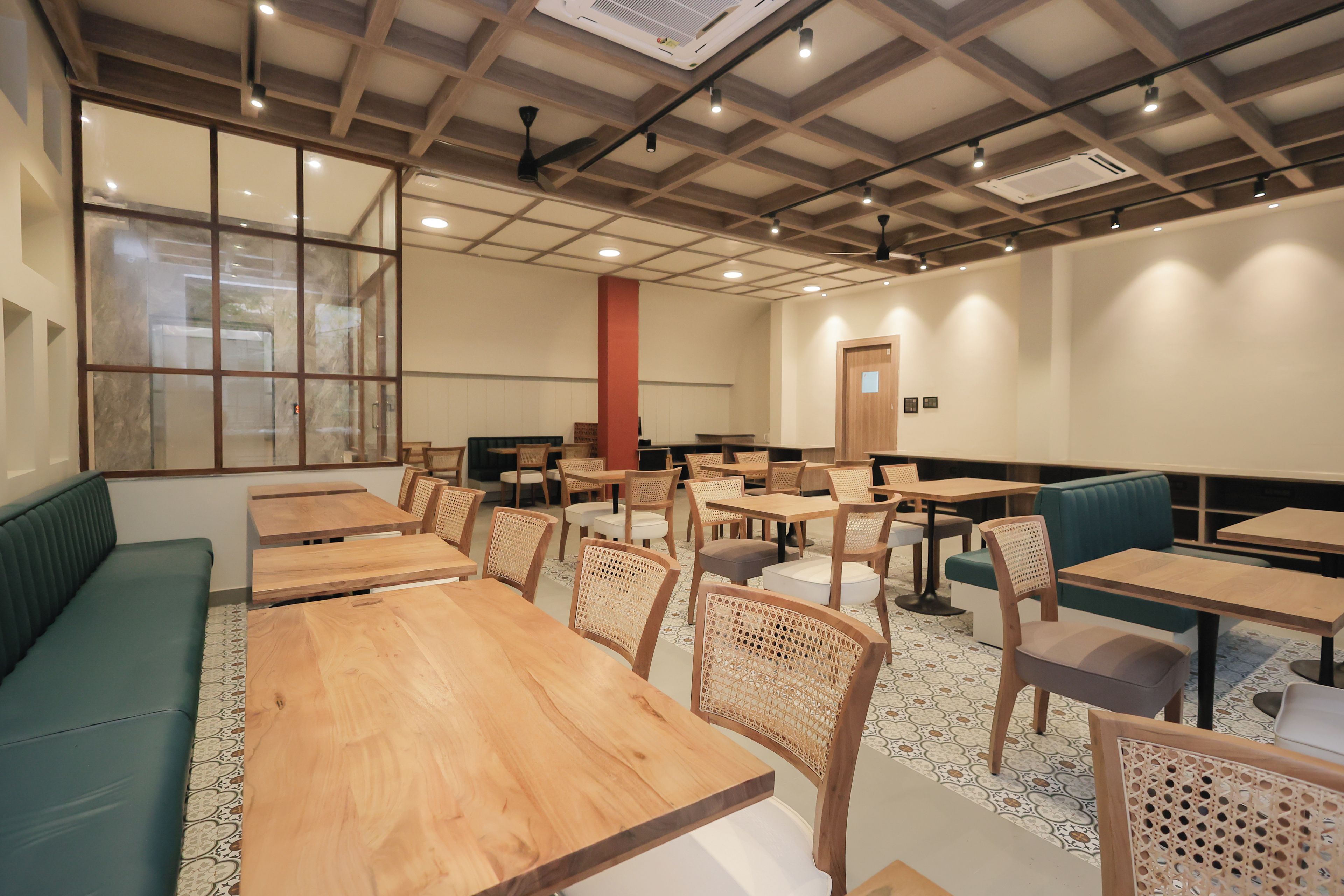 A restaurant interior with wooden tables and chairs, a green sofa, and patterned flooring.