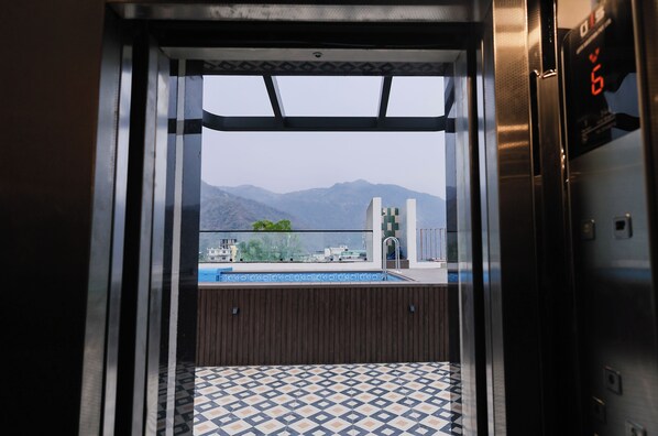 An elevator with a view of a swimming pool and mountains in the background.