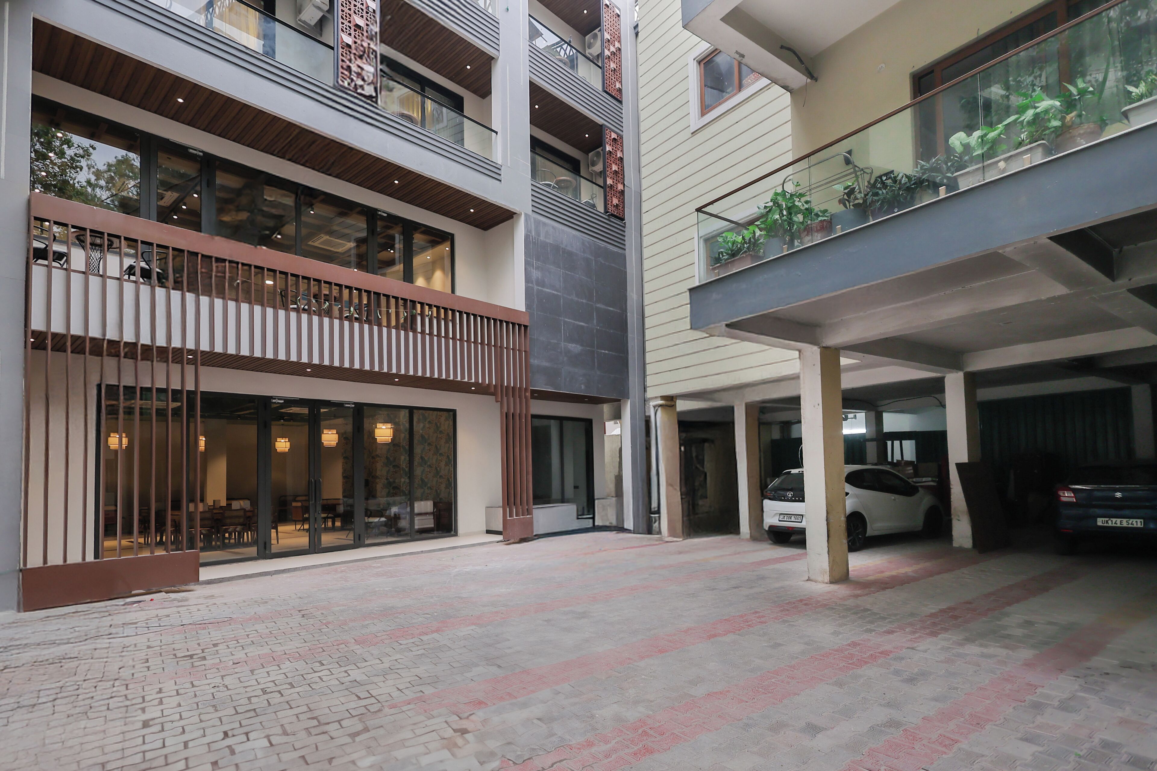 A multi-level building with a covered parking area, glass railings, and potted plants.