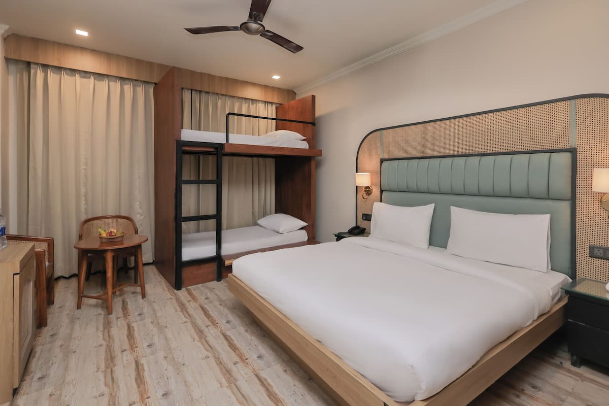 A hotel room with a bunk bed, a desk with a chair, a bedside table with a lamp, and a ceiling fan.