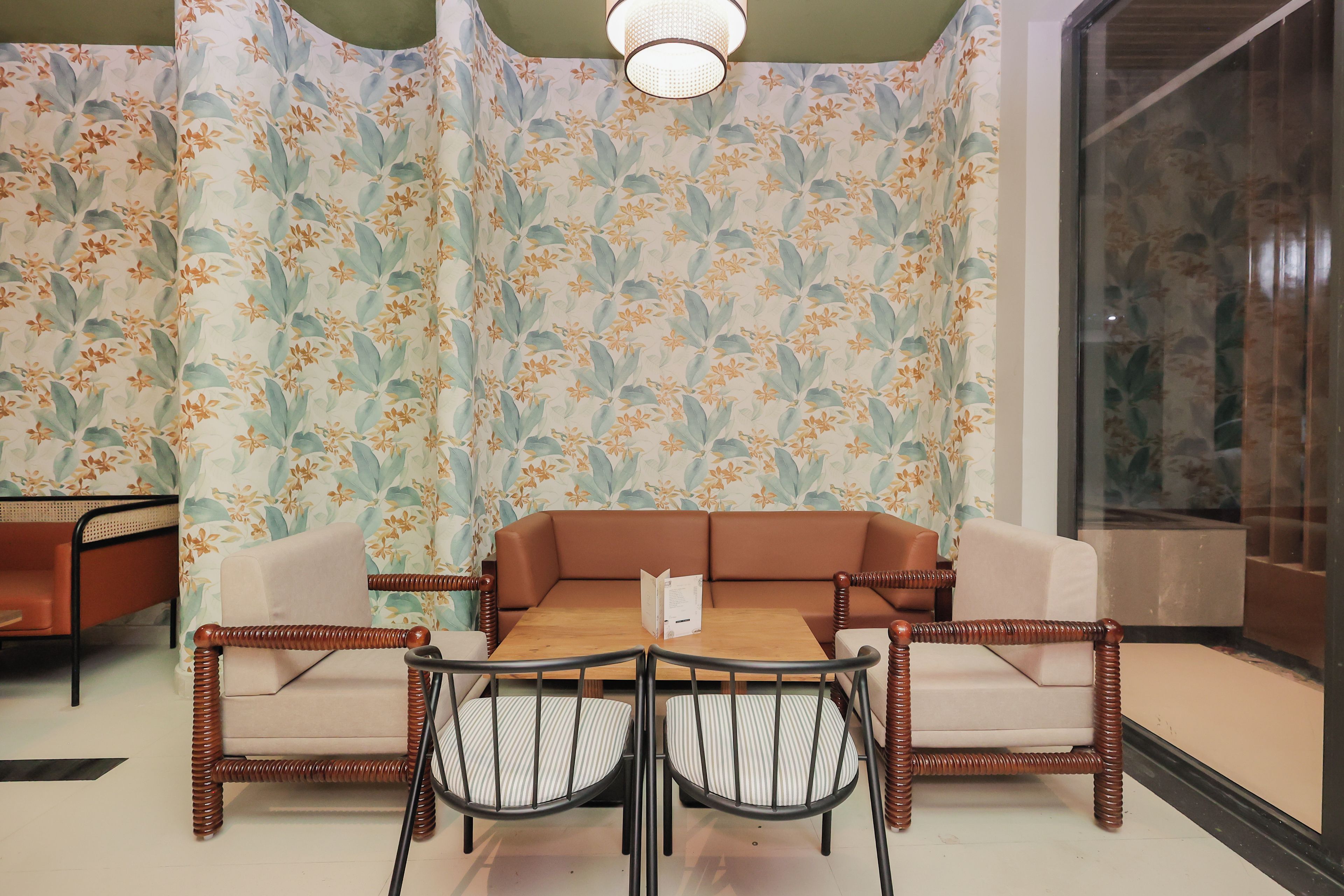 A room with a floral wallpaper, a brown sofa, a wooden table with chairs, and a hanging light fixture.