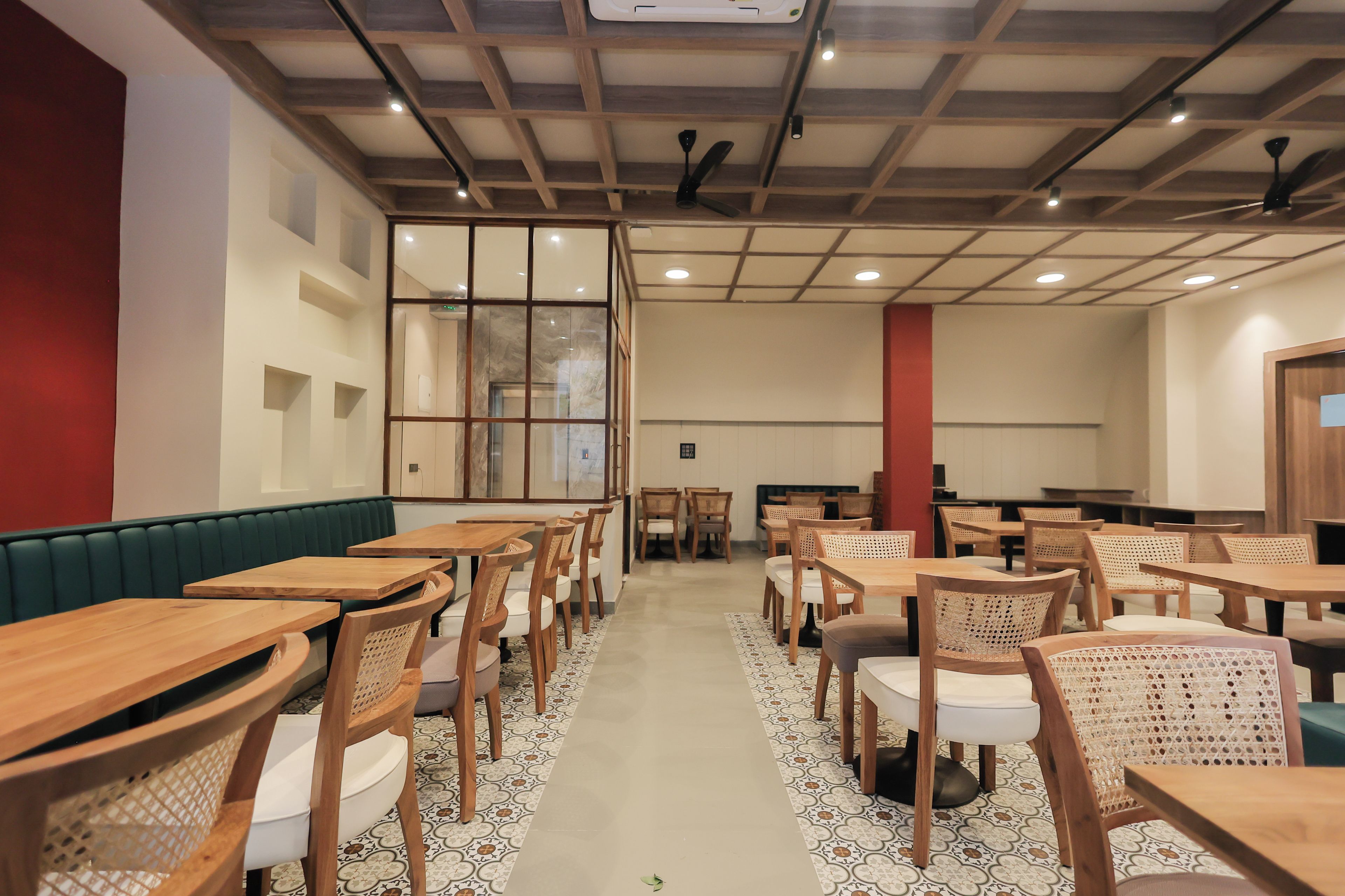A spacious dining area with multiple wooden tables and chairs, a high ceiling with exposed beams, and a patterned floor.