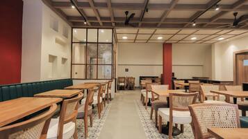 A spacious dining area with multiple wooden tables and chairs, a high ceiling with exposed beams, and a patterned floor.