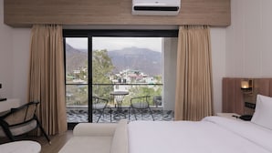 Een hotelkamer met een groot bed, een bureau, een stoel en uitzicht op bergen door een groot raam.