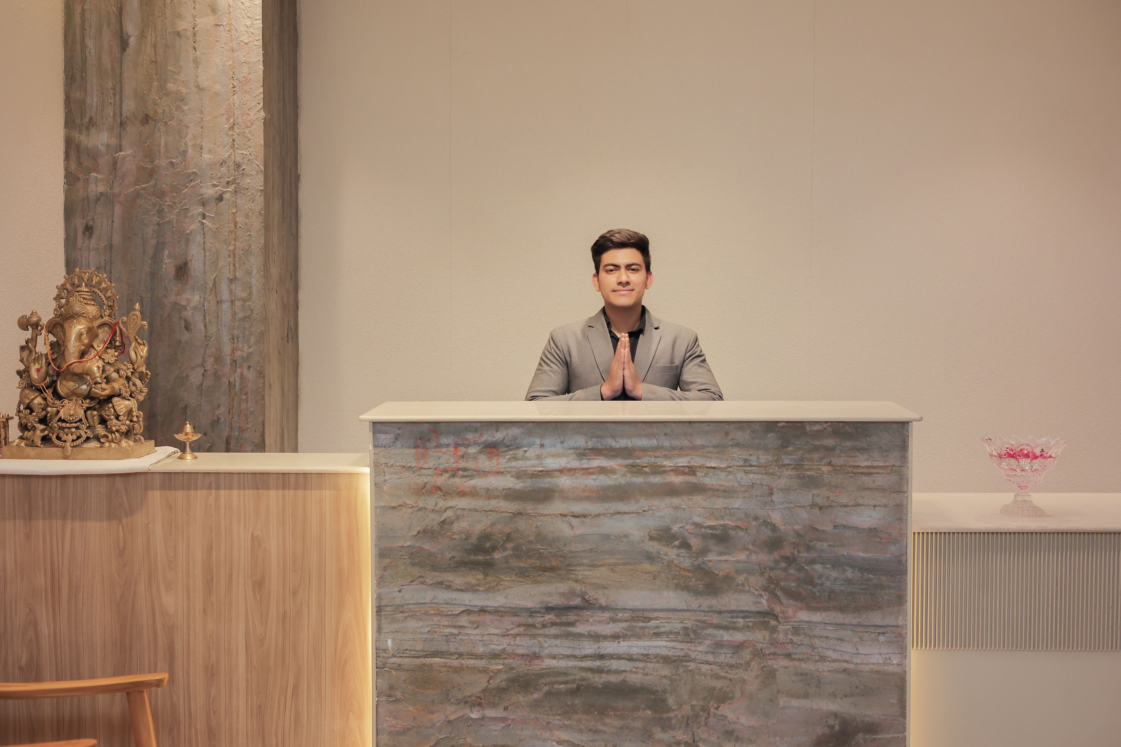 A person seated at a podium with a textured wall behind.