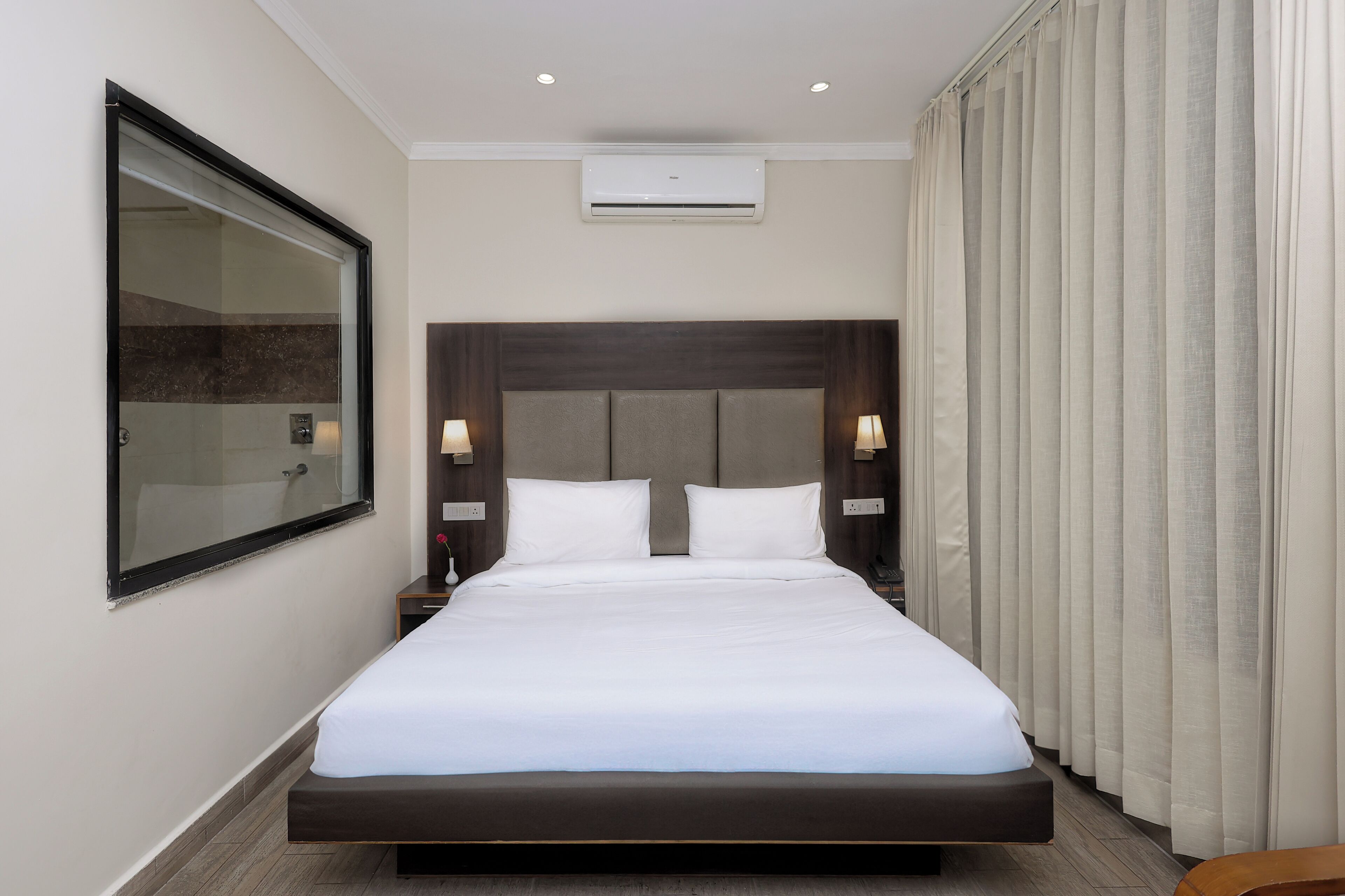 A modern hotel room with a large bed, a glass shower enclosure, and a view of the cityscape.