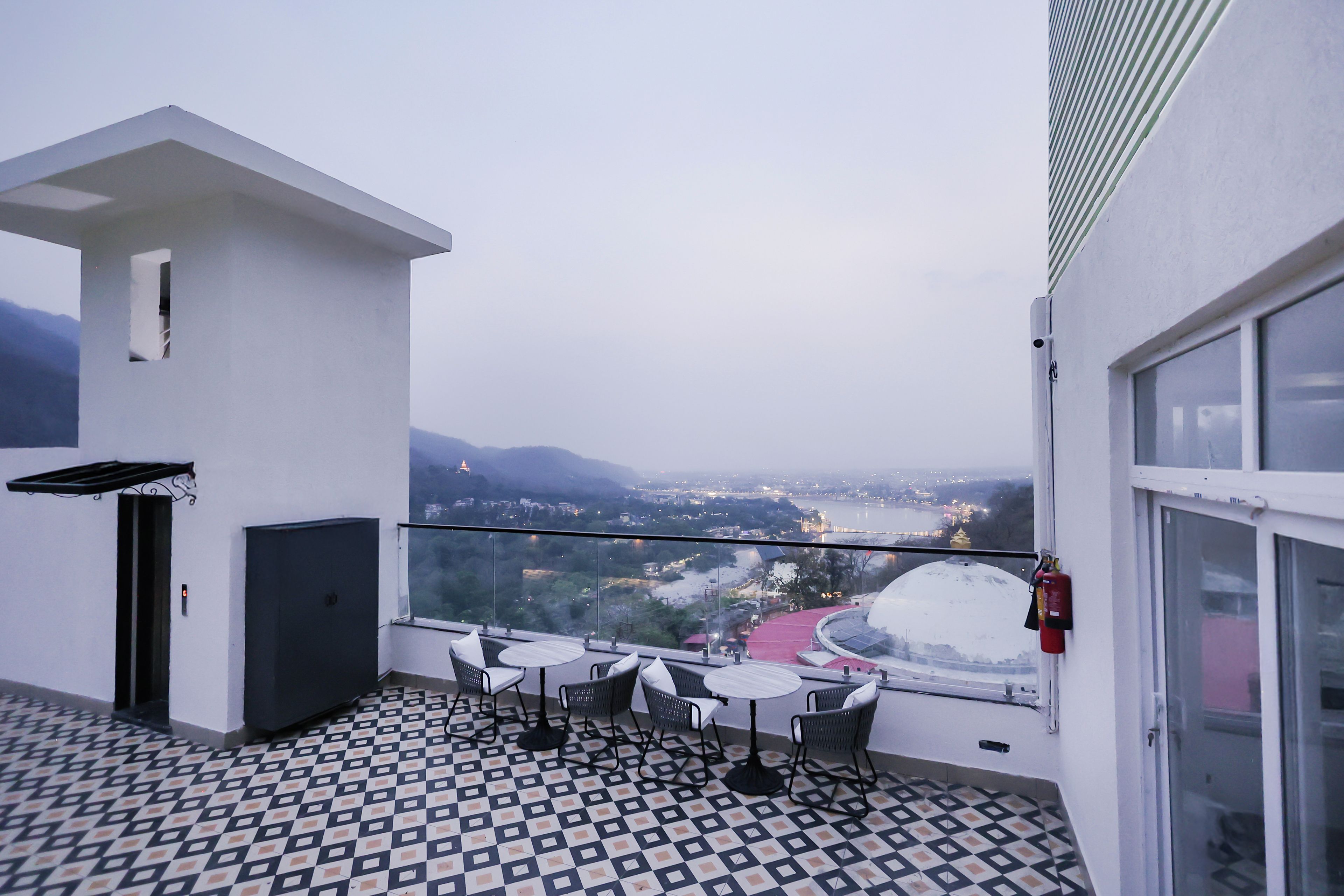 Ein Balkon mit gemustertem Boden, einem Tisch mit Stühlen und Blick auf eine Stadtlandschaft mit Bergen im Hintergrund.