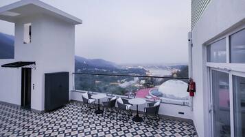 Ein Balkon mit gemustertem Boden, einem Tisch mit Stühlen und Blick auf eine Stadtlandschaft mit Bergen im Hintergrund.