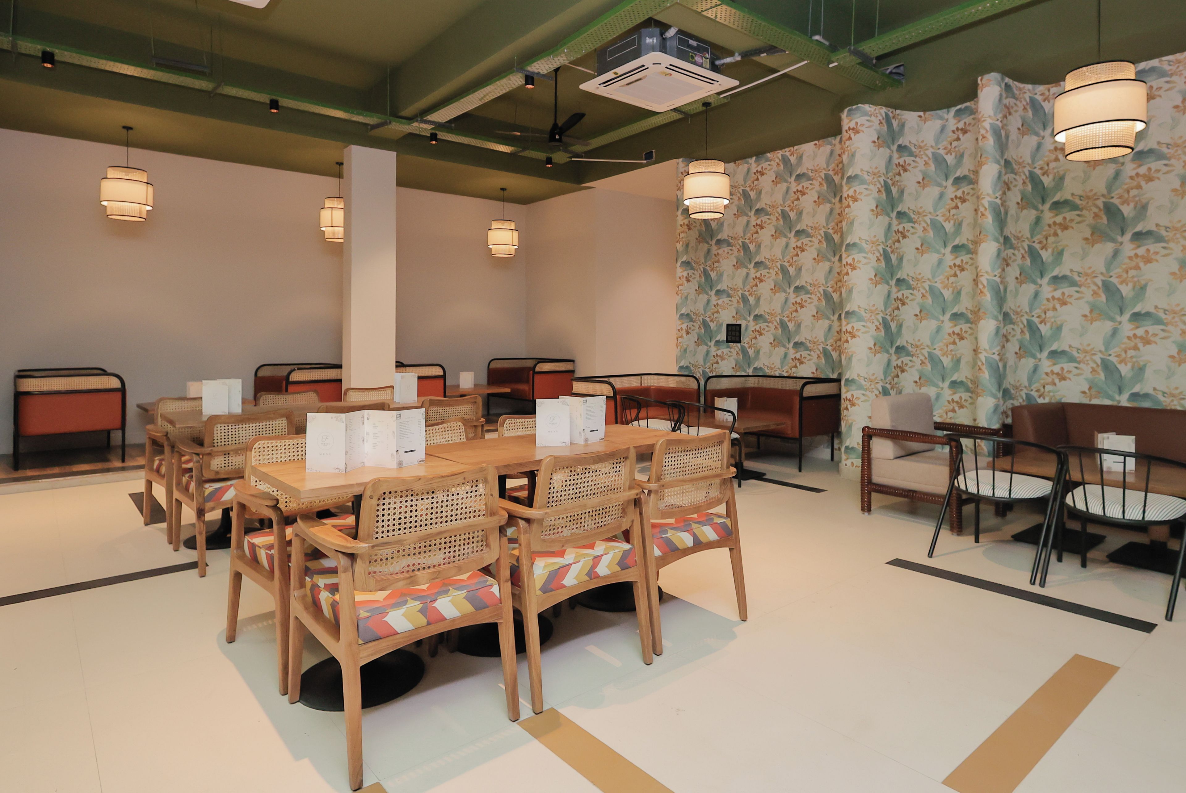 A restaurant with wooden tables and chairs, a high ceiling with exposed beams, and a floral wallpaper on one wall.