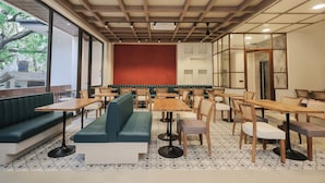 Een restaurantinterieur met houten tafels en stoelen, groene zachte zitplaatsen en een rode accentmuur.