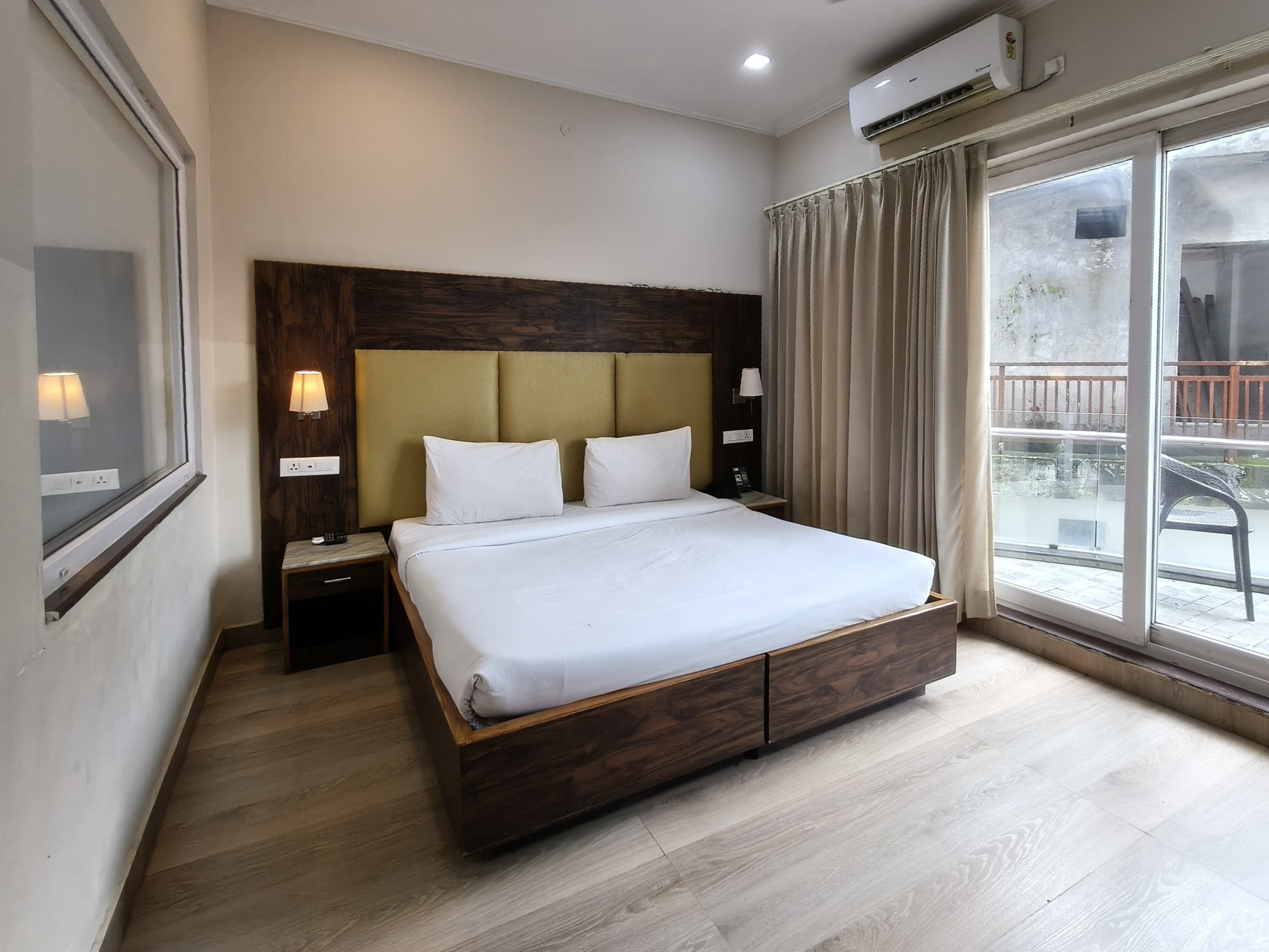 Ein Hotelzimmer mit einem großen Bett, einem Holzkopfschild, einem Nachttisch mit Lampe und einem Fenster mit Vorhängen.