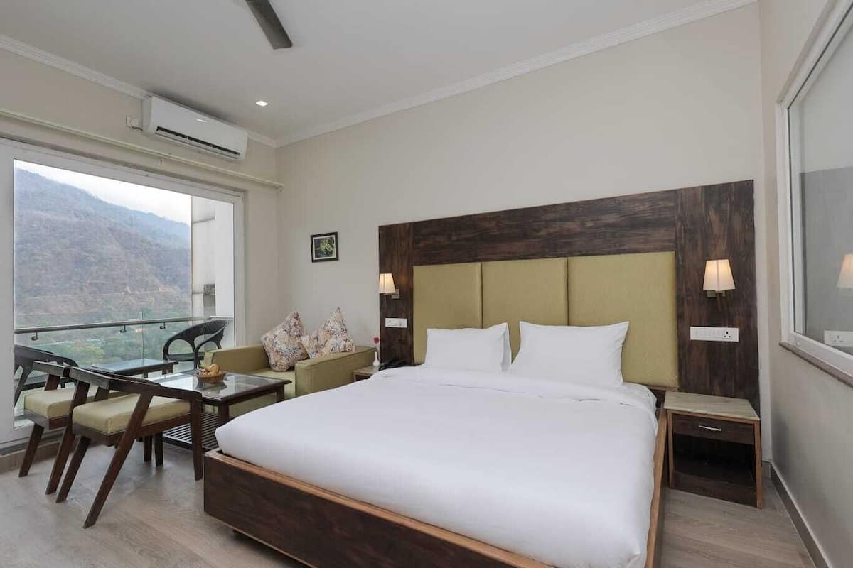 A hotel room with a large bed, a desk, and a chair. There is a window with a mountain view.