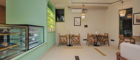 A cafe interior with a display case, tables, chairs, and a wall-mounted air conditioner.