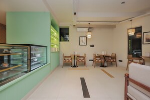 Interior de una cafetería con una vitrina, mesas, sillas y un aire acondicionado instalado en la pared.