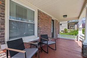 Eine überdachte Veranda mit zwei Stühlen und einem Tisch, Ziegelmauern und Blick auf ein Nachbarhaus.