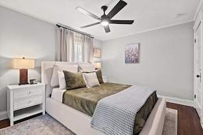 Ein Schlafzimmer mit Bett, Nachttisch, Lampe, Deckenventilator und Kunstwerk an der Wand.