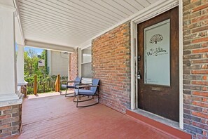 A covered porch with a brick wall, a door with a sign, and outdoor furniture.