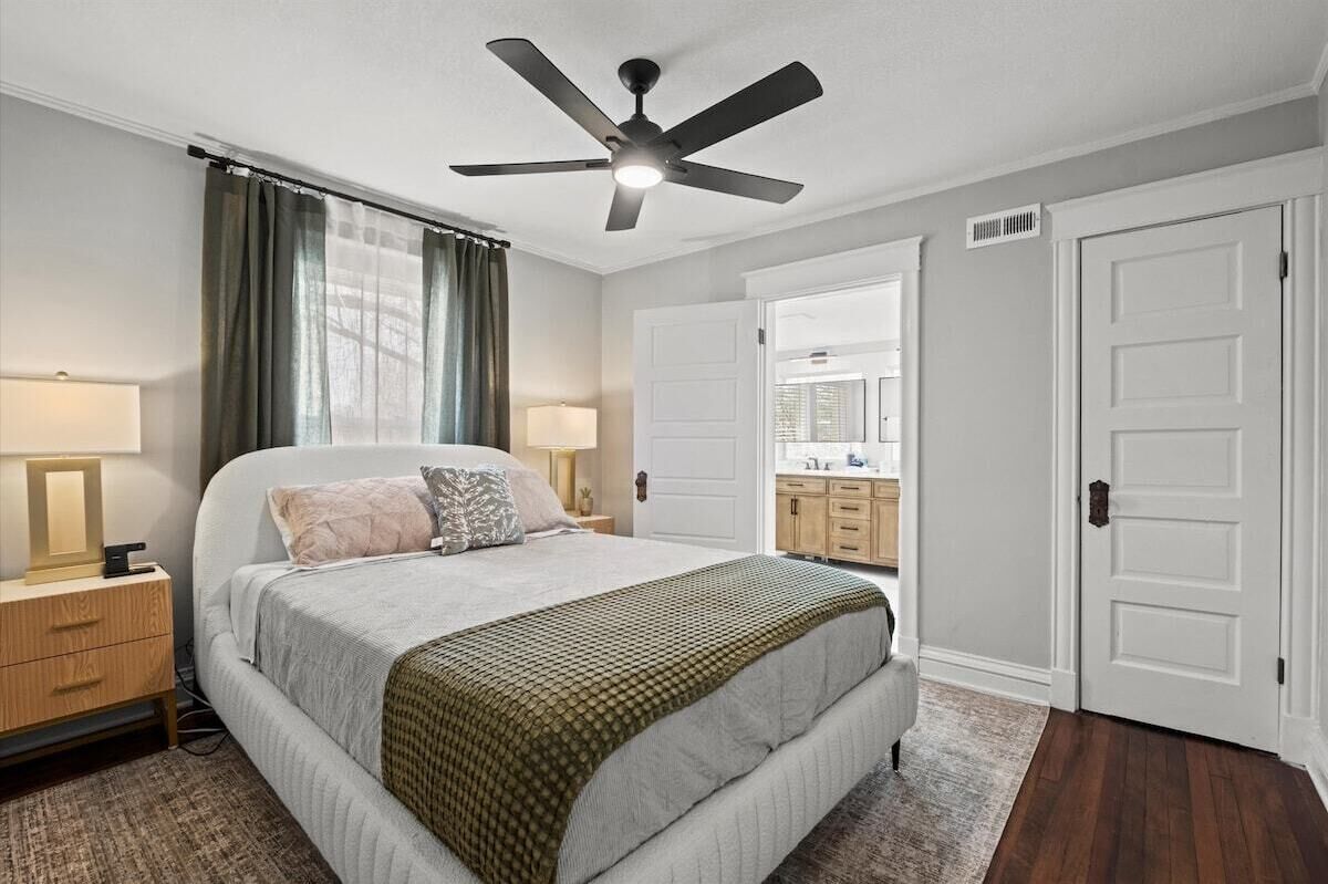 Cozy queen bedroom with en suite bathroom, featuring warm wood floors, soft layered bedding, and modern lighting for a relaxing retreat. Located on the second floor.