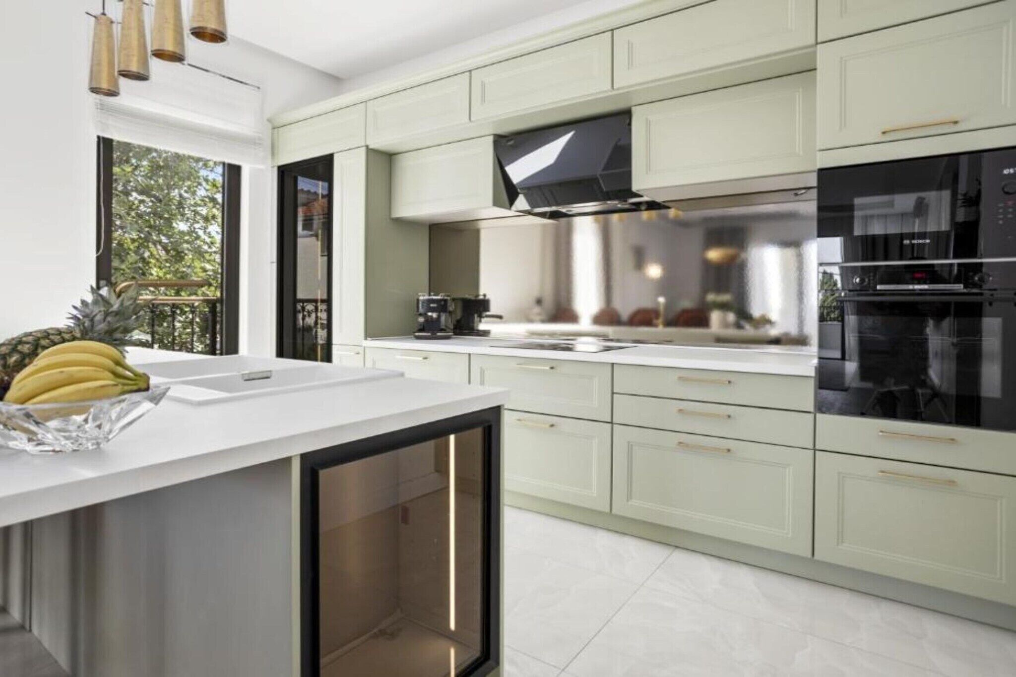 A modern kitchen with light green cabinets, a white countertop, and stainless steel appliances.