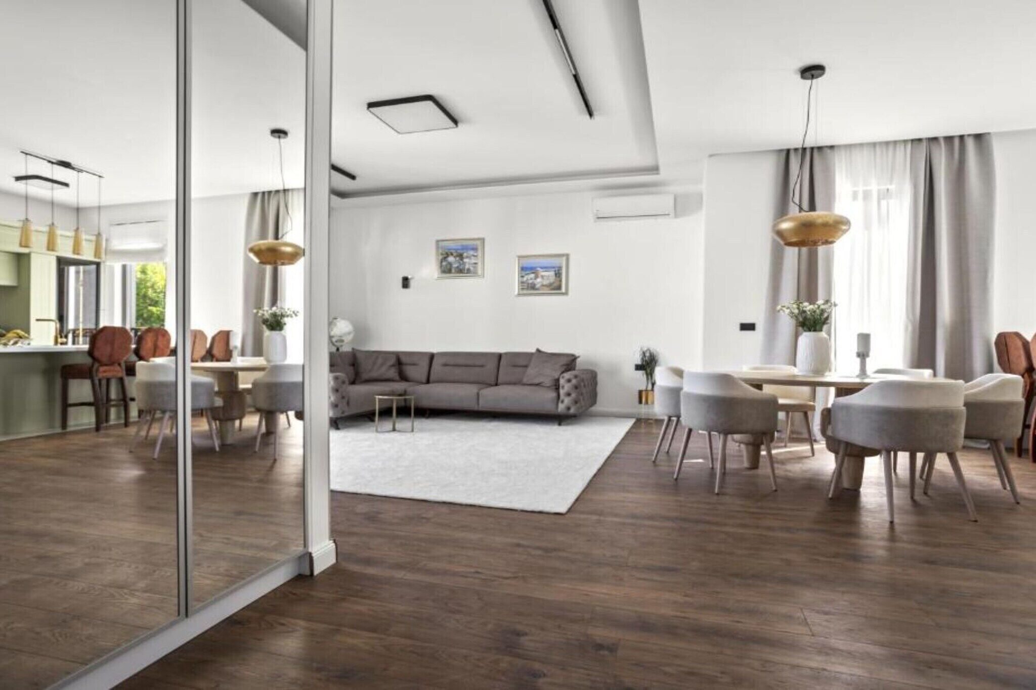 A modern living room with a grey sofa, a dining area with a white table, and a kitchen in the background.