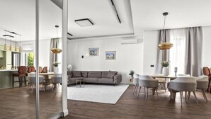 A modern living room with a grey sofa, a dining area with a white table, and a kitchen in the background. - Three-Bedroom Penthouse Apartment (Omis)