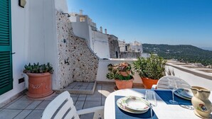 A terrace with a table set for two, potted plants, and a clear view of the landscape. - Palazzo Bellavista by Rentbeat (Ostuni)