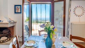 A dining table set with plates, glasses, and a vase with flowers, with a view of the sea through a glass door. - Palazzo Bellavista by Rentbeat (Ostuni)