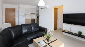 Un salon moderne avec un canapé en cuir noir, une table basse dotée d’une télécommande et un téléviseur à écran plat fixé au mur.