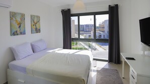 Une chambre à coucher avec un lit, un bureau, une télévision et une fenêtre avec des rideaux.