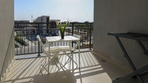 Un balcon avec une table et des chaises blanches, un pot de fleurs et une vue sur le paysage urbain.